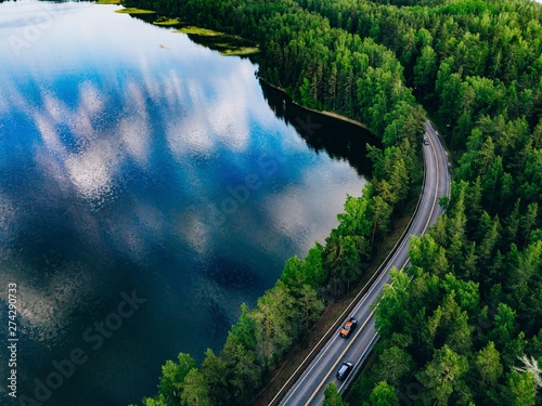 Aerial view of road between green forest and blue lake in Finland