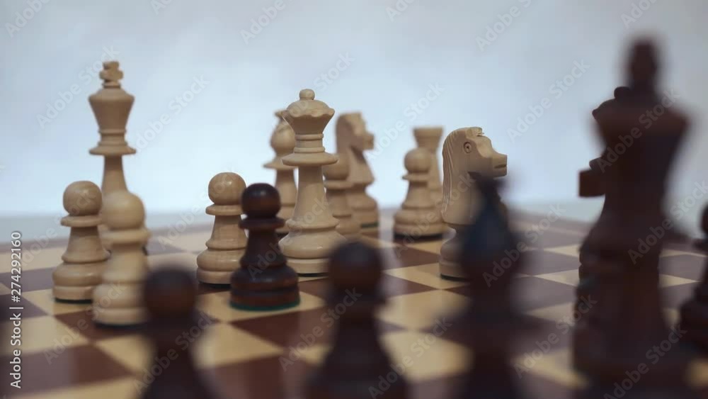 Black And White Wooden Chess On Chessboard In Starting Positions Ready For The Game. White Background. Closeup. Horyzontal movement of the camera, dolly shot. Black And White Wooden Chess On Chessboard In Starting Positions Ready For The Game. White Background. Closeup. Horyzontal movement of the camera, dolly shot.