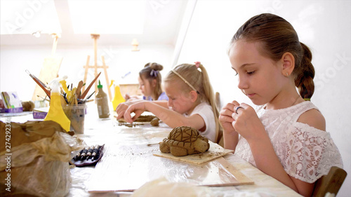 Children are sculpting toys from wet clay. They are using special tools under the guidance of a teacher on art lesson in workshop in elementary school.
