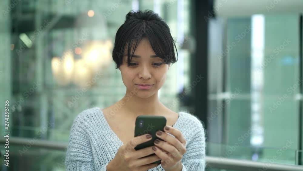Portrait pan shot slow motion of smiling happy black hair asian female wearing grey sweatshirt typing on phone. Freelance concept Portrait pan shot slow motion of smiling happy black hair asian female wearing grey sweatshirt typing on phone. Freelance concept