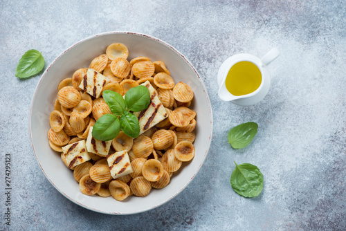 Orecchiette pasta with slices of grilled cheese and fresh green basil, flatlay on a light-grey stone background