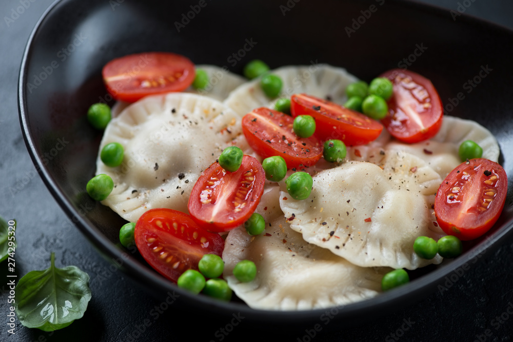 Closeup of a black bowl with ravioli, cherry tomatoes and green peas, selective focus Closeup of a black bowl with ravioli, cherry tomatoes and green peas, selective focus