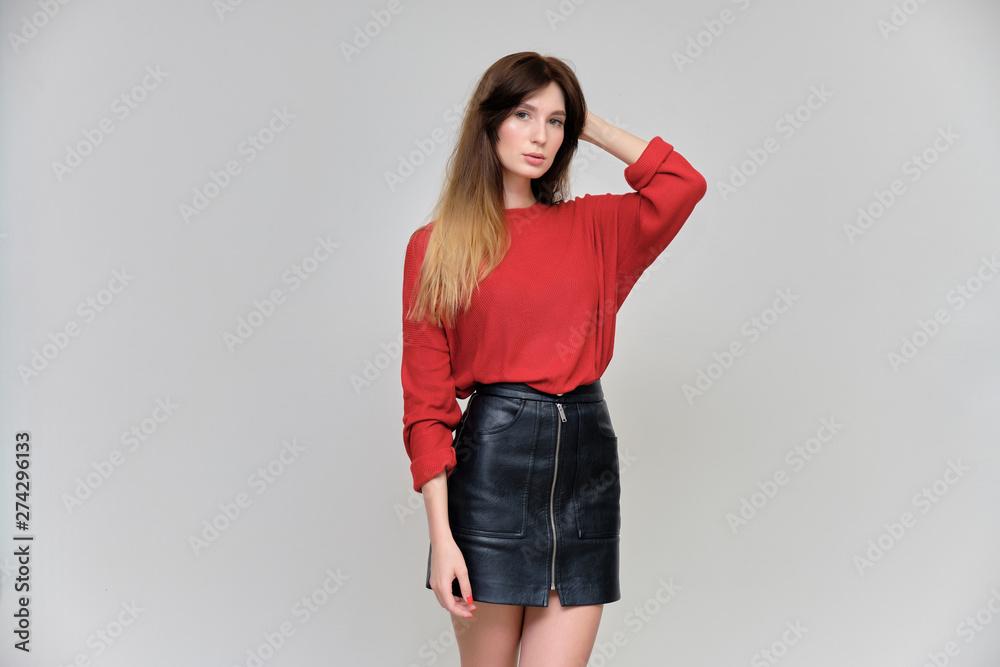 Photo portrait of a beautiful pretty brunette girl in a red sweater on a gray background. A woman is satisfied with her life, she stands in front of the camera, smiling and talking. Made in a studio. Photo portrait of a beautiful pretty brunette girl in a red sweater on a gray background. A woman is satisfied with her life, she stands in front of the camera, smiling and talking. Made in a studio.