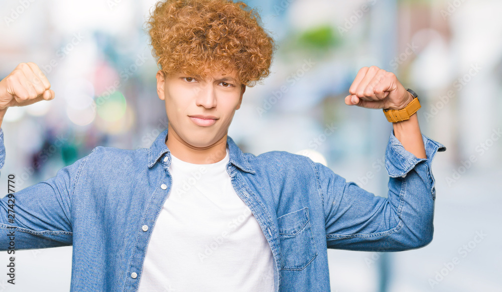 Young handsome man with afro hair wearing denim jacket showing arms muscles smiling proud. Fitness concept. Young handsome man with afro hair wearing denim jacket showing arms muscles smiling proud. Fitness concept.