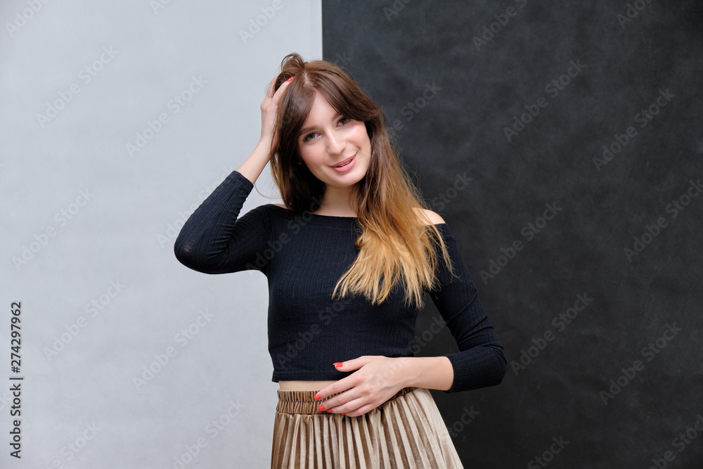 Fototapeta premium Beauty portrait of a beautiful pretty brunette girl in a black sweater on a two-color background. A woman is happy with life, stands in front of the camera, smiles. Made in a studio.