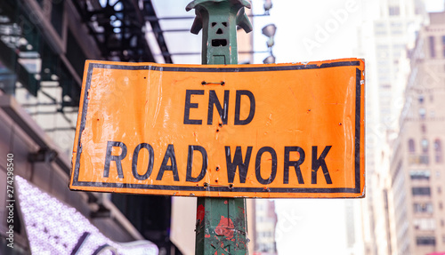 End Road Work. Warning sign, orange color, blur buildings background