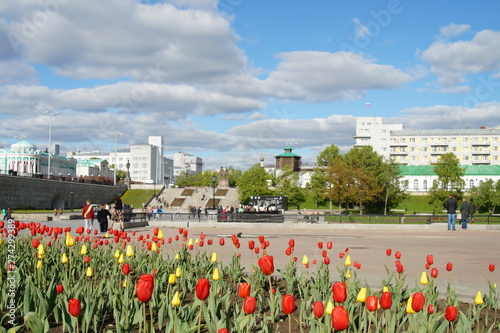 Red and yellow tulips on the background of the cityscape with clouds, blue sky in the historic quarter of Yekaterinburg. 