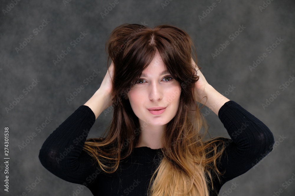 Beauty portrait of a beautiful pretty brunette girl in a black sweater on a dark gray background. A woman is happy with life, she is standing in front of the camera, smiling. Made in a studio. Beauty portrait of a beautiful pretty brunette girl in a black sweater on a dark gray background. A woman is happy with life, she is standing in front of the camera, smiling. Made in a studio.