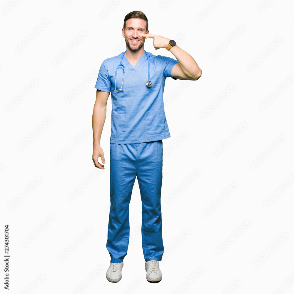 Fototapeta premium Handsome doctor man wearing medical uniform over isolated background Pointing with hand finger to face and nose, smiling cheerful