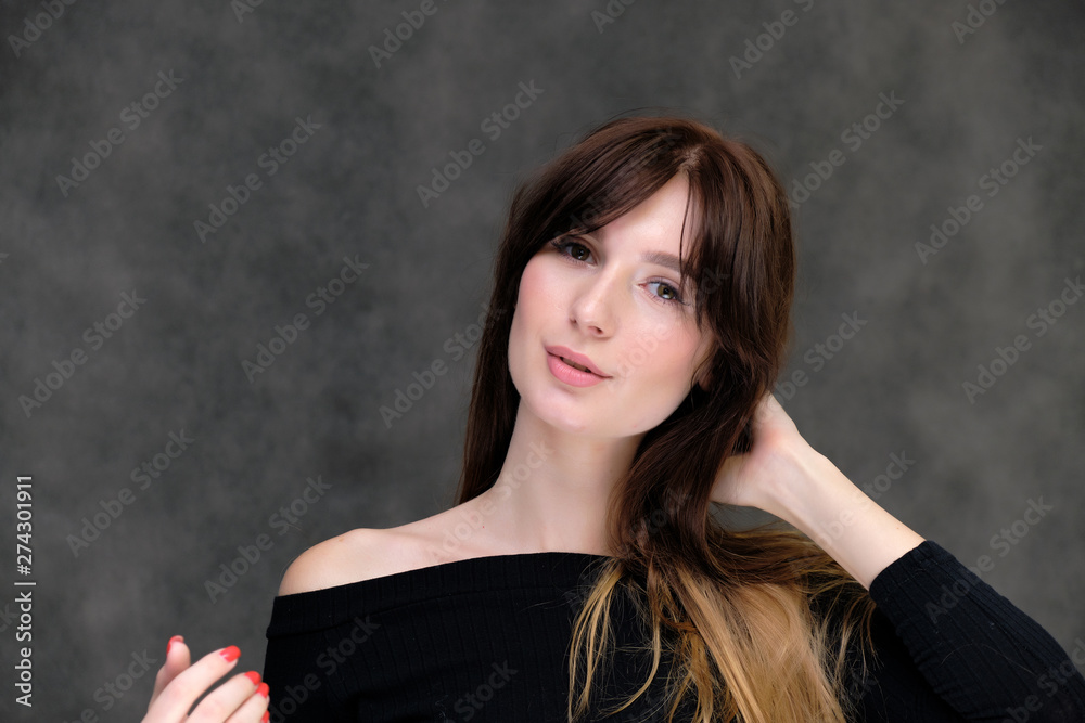 Beauty portrait of a beautiful pretty brunette girl in a black sweater on a dark gray background. A woman is happy with life, she is standing in front of the camera, smiling. Made in a studio. Beauty portrait of a beautiful pretty brunette girl in a black sweater on a dark gray background. A woman is happy with life, she is standing in front of the camera, smiling. Made in a studio.