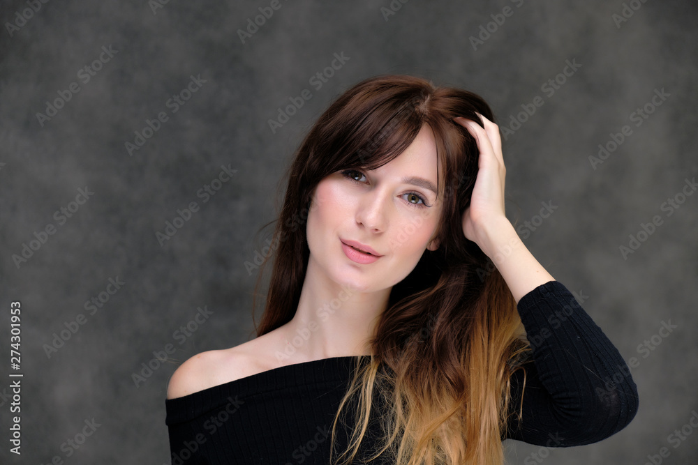 Beauty portrait of a beautiful pretty brunette girl in a black sweater on a dark gray background. A woman is happy with life, she is standing in front of the camera, smiling. Made in a studio.