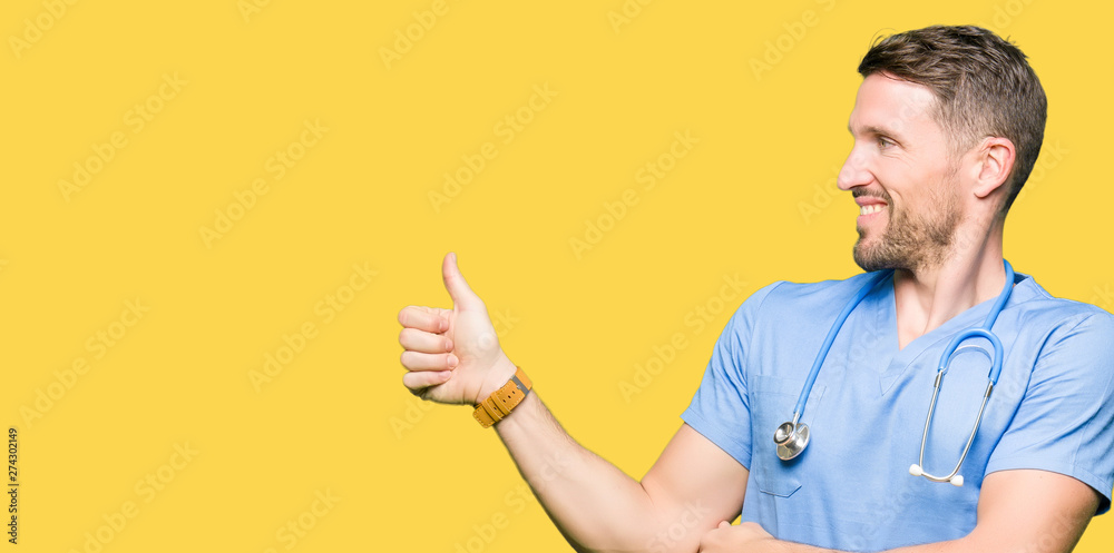 Handsome doctor man wearing medical uniform over isolated background Looking proud, smiling doing thumbs up gesture to the side Handsome doctor man wearing medical uniform over isolated background Looking proud, smiling doing thumbs up gesture to the side