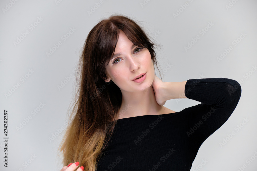 Beauty portrait of a beautiful pretty brunette girl in a black sweater on a light gray background. A woman is happy with life, she is standing in front of the camera, smiling. Made in a studio. Beauty portrait of a beautiful pretty brunette girl in a black sweater on a light gray background. A woman is happy with life, she is standing in front of the camera, smiling. Made in a studio.