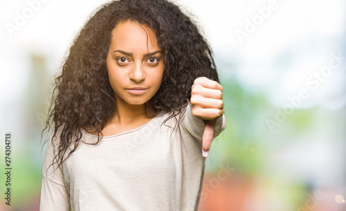 Young beautiful girl with curly hair wearing casual sweater looking unhappy and angry showing rejection and negative with thumbs down gesture. Bad expression. © Krakenimages.com
