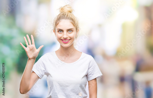 Young beautiful blonde woman wearing white t-shirt over isolated background showing and pointing up with fingers number five while smiling confident and happy.