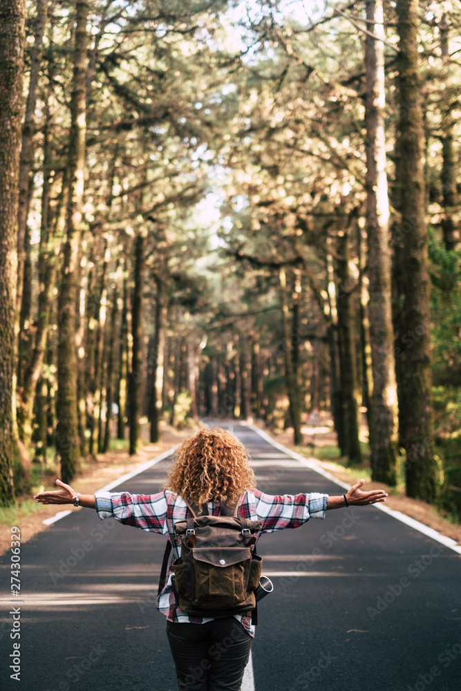 Alternative travel concept with curly hipster woman viewed from back open his arms and feel the freedom of the outdoors nature standing in the middle of a ling road - happiness and lifestyle