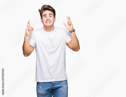 Young handsome man wearing white t-shirt over isolated background smiling crossing fingers with hope and eyes closed. Luck and superstitious concept.