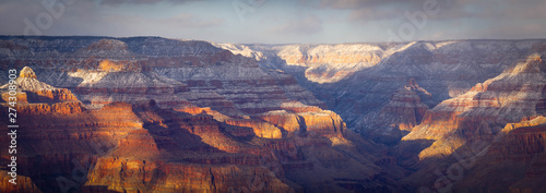 An evening winter panorama of the Grand Canyon with snow in the high elevation and dramatic sunlight and shadows being cast into the canyon.
