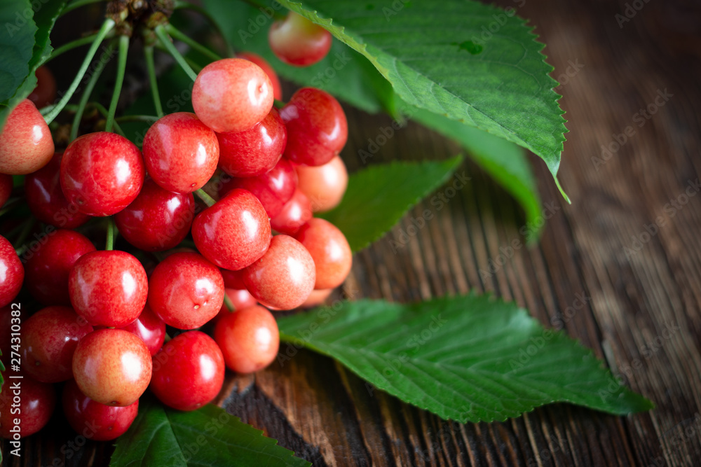 Cherry fresh red berries, and green leaves on a wooden background Cherry fresh red berries, and green leaves on a wooden background
