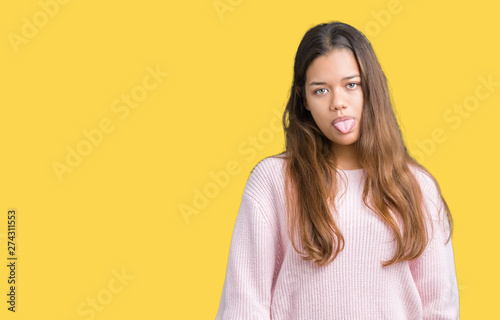 Young beautiful brunette woman wearing pink winter sweater over isolated background sticking tongue out happy with funny expression. Emotion concept. © Krakenimages.com