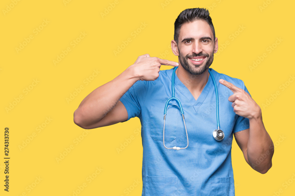 Handsome young doctor surgeon man over isolated background smiling confident showing and pointing with fingers teeth and mouth. Health concept. Handsome young doctor surgeon man over isolated background smiling confident showing and pointing with fingers teeth and mouth. Health concept.