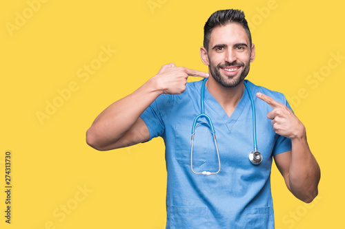 Handsome young doctor surgeon man over isolated background smiling confident showing and pointing with fingers teeth and mouth. Health concept.