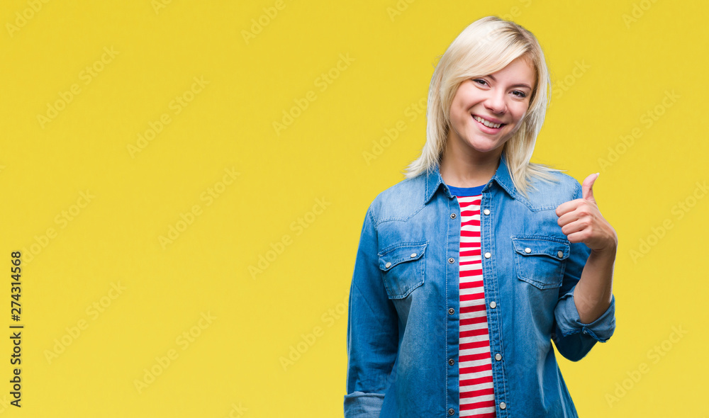 Young beautiful blonde woman wearing denim jacket over isolated background doing happy thumbs up gesture with hand. Approving expression looking at the camera with showing success. Young beautiful blonde woman wearing denim jacket over isolated background doing happy thumbs up gesture with hand. Approving expression looking at the camera with showing success.