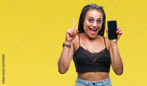 Young braided hair african american with birth mark showing smartphone screen over isolated background surprised with an idea or question pointing finger with happy face, number one