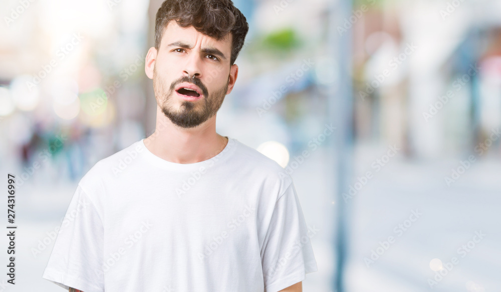 Young handsome man wearing white t-shirt over isolated background In shock face, looking skeptical and sarcastic, surprised with open mouth Young handsome man wearing white t-shirt over isolated background In shock face, looking skeptical and sarcastic, surprised with open mouth