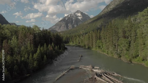Flight through river and evergreen forest with rocky mountain peak in background, slow forward tracking shot