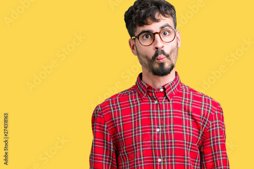 Young handsome man wearing glasses over isolated background making fish face with lips, crazy and comical gesture. Funny expression.