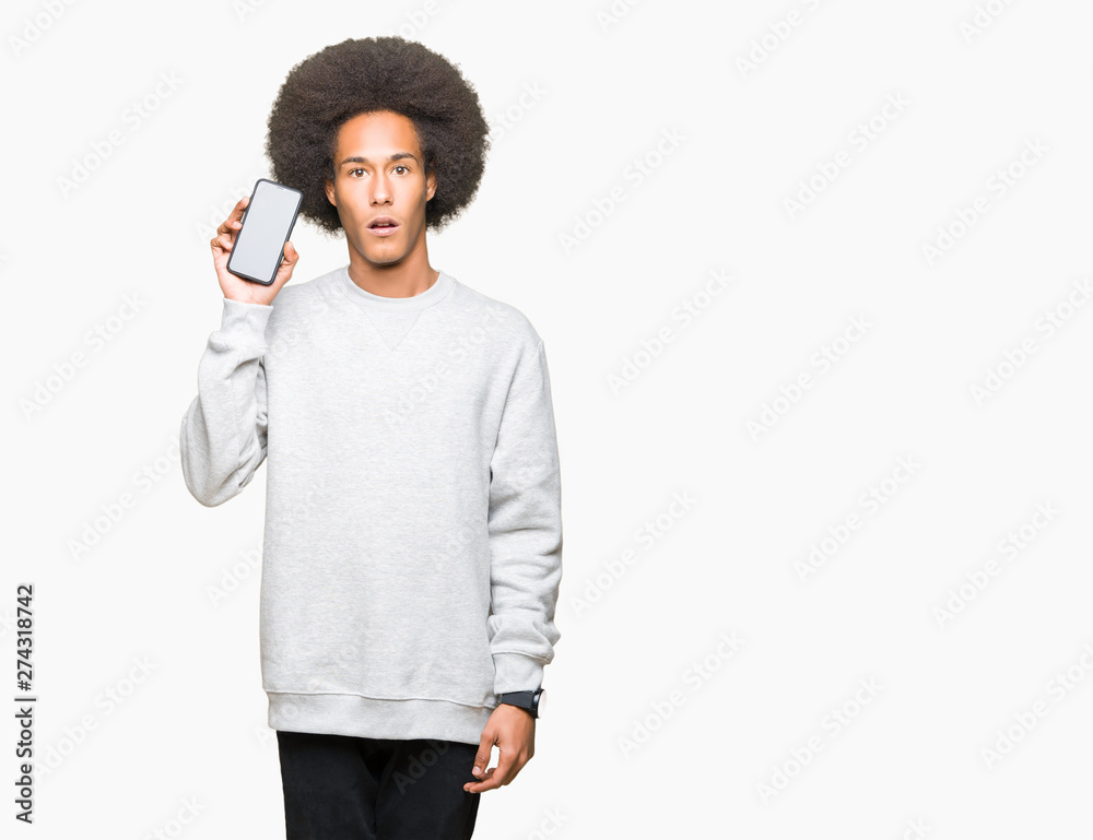 Young african american man with afro hair showing smartphone screen scared in shock with a surprise face, afraid and excited with fear expression Young african american man with afro hair showing smartphone screen scared in shock with a surprise face, afraid and excited with fear expression