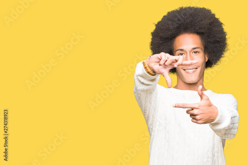Young african american man with afro hair wearing winter sweater smiling making frame with hands and fingers with happy face. Creativity and photography concept.