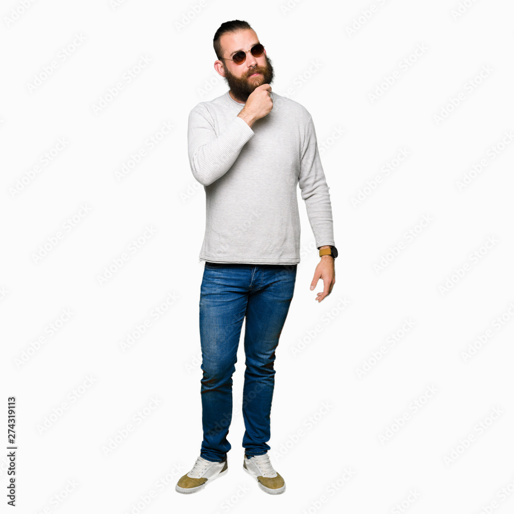 Young hipster man wearing sunglasses with hand on chin thinking about question, pensive expression. Smiling with thoughtful face. Doubt concept. Young hipster man wearing sunglasses with hand on chin thinking about question, pensive expression. Smiling with thoughtful face. Doubt concept.