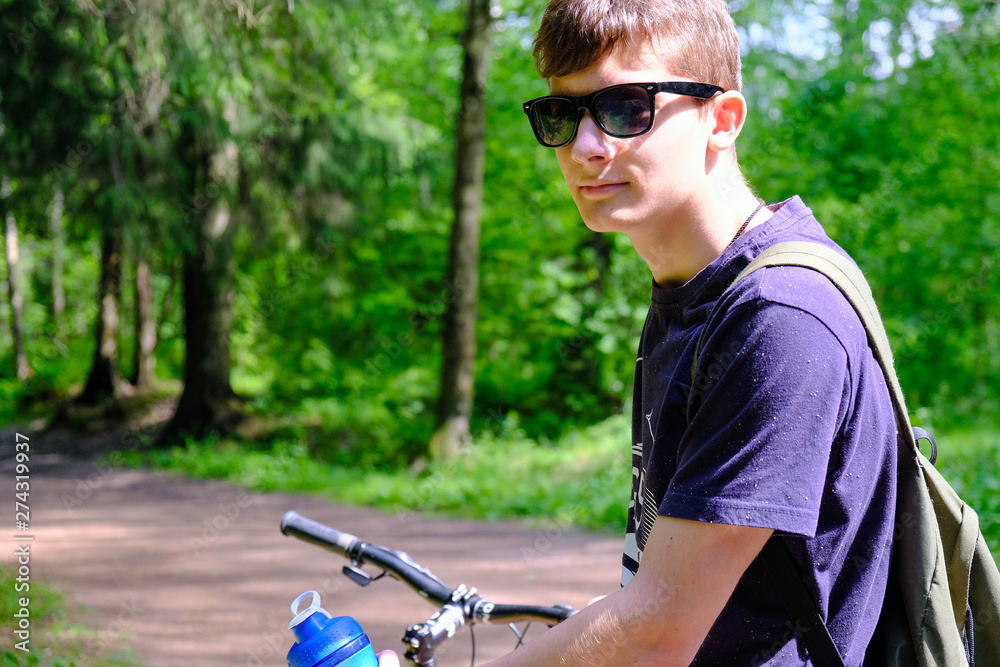 Naklejka premium Young man sitting on the mountain near the bike. He looks dreamily into the distance. Sports lifestyle.