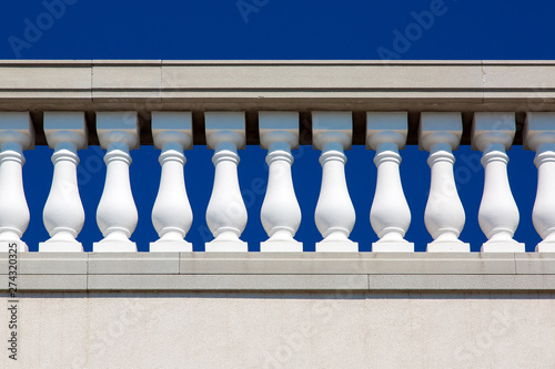 Baroque architecture details of stone railings with white balustrades close up against a blue sky.