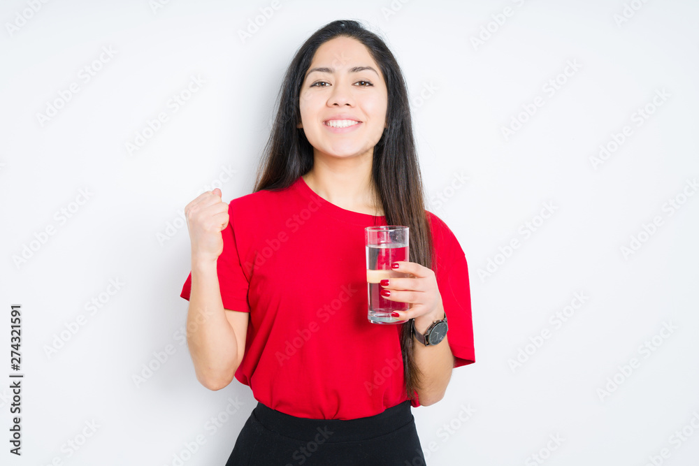 Young brunette woman drinking a glass of water over isolated background screaming proud and celebrating victory and success very excited, cheering emotion Young brunette woman drinking a glass of water over isolated background screaming proud and celebrating victory and success very excited, cheering emotion