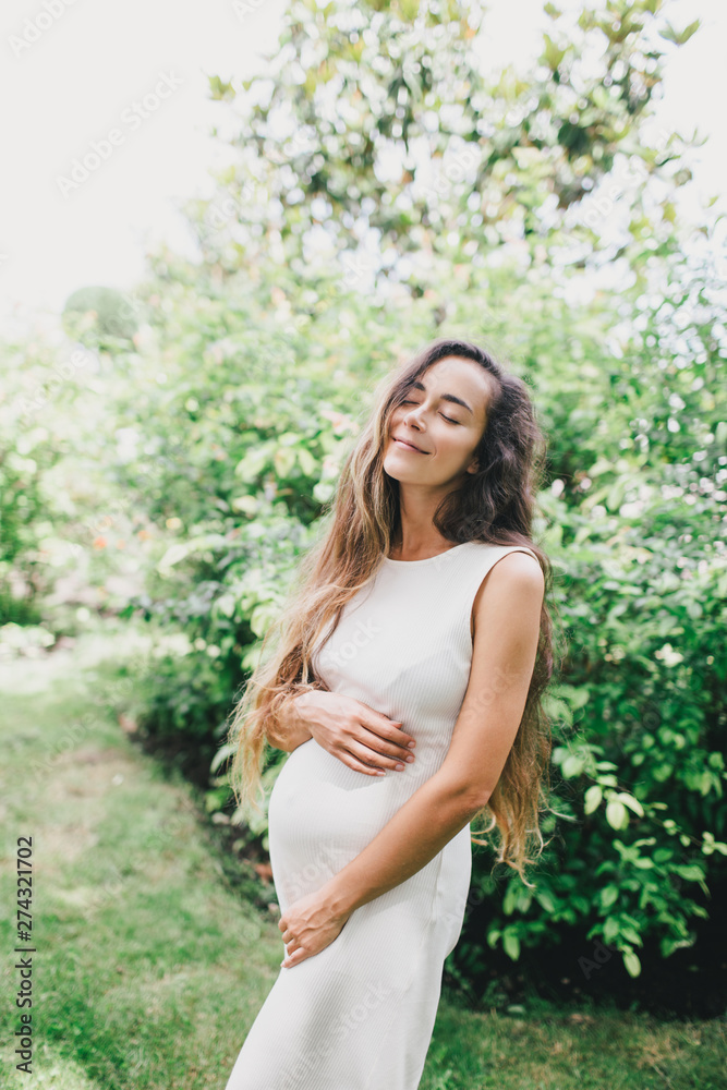 Young beautiful pregnant woman with long healthy curly hair posing in a green park outdoors. Young beautiful pregnant woman with long healthy curly hair posing in a green park outdoors.