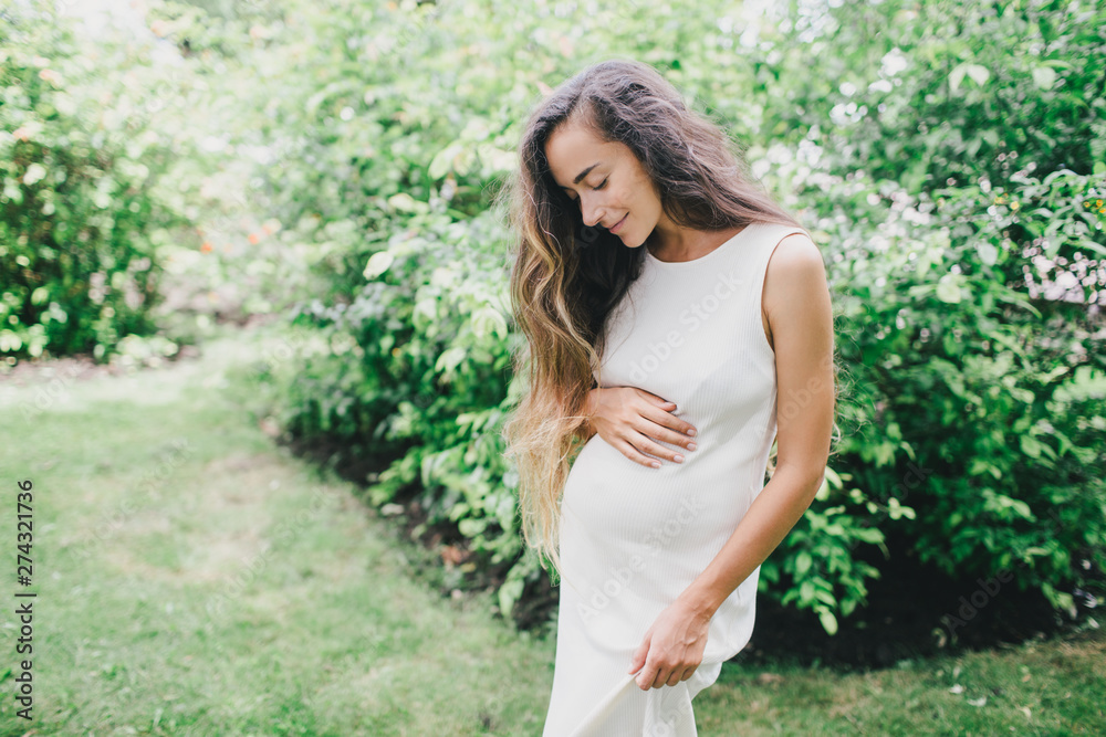 Young beautiful pregnant woman with long healthy curly hair posing in a green park outdoors. Young beautiful pregnant woman with long healthy curly hair posing in a green park outdoors.