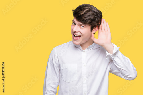 Young handsome business man over isolated background smiling with hand over ear listening an hearing to rumor or gossip. Deafness concept.