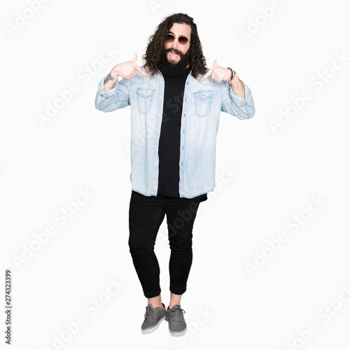 Young hipster man with long hair and beard wearing sunglasses looking confident with smile on face, pointing oneself with fingers proud and happy. © Krakenimages.com