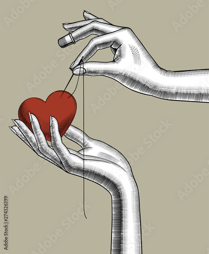 Female hands with a needle and a red sewing pad in the shape of heart