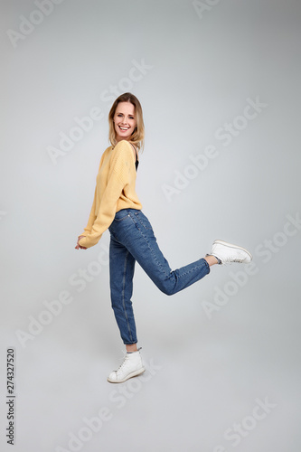 Feeling comfortable in her style. Full length studio shot of attractive young woman in casual wear smiling and looking away while jumping against grey background