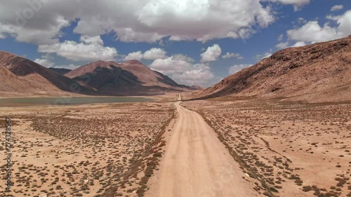 Aerial over gravel off road trail near arid desert mountains in sunny day.Pamir highway silk road trip adventure in Kyrgyzstan and Tajikistan desert,central Asia.4k drone flight establisher video