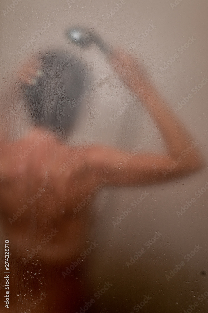 The woman behind the glass washes in the shower stall.