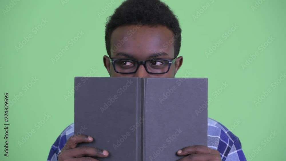 Shy young African hipster man thinking while hiding behind book Shy young African hipster man thinking while hiding behind book
