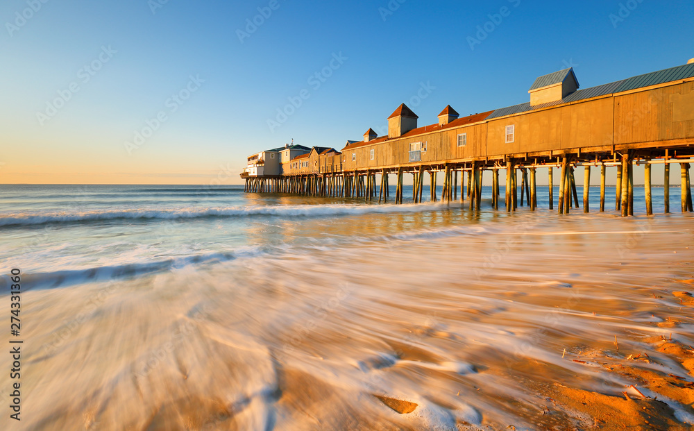 Fototapeta premium Beautiful sunrise over Old Orchard Beach Pier, Saco Maine USA. The wooden pier on the beach contains many other tourist businesses, including a variety of souvenir shops.