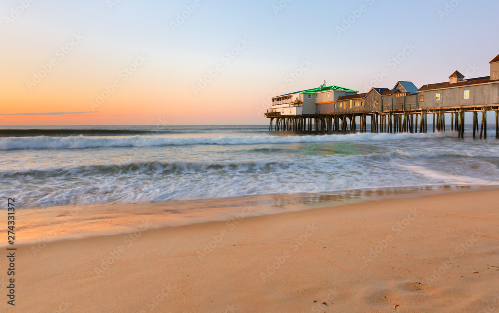 Naklejka premium Beautiful sunrise over Old Orchard Beach Pier, Saco Maine USA. The wooden pier on the beach contains many other tourist businesses, including a variety of souvenir shops.