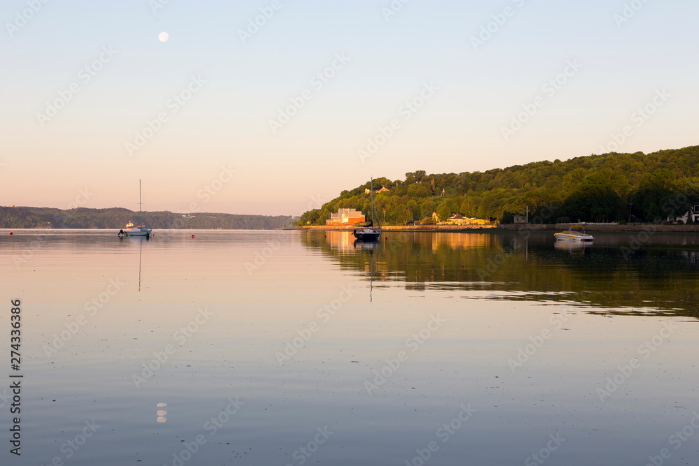 Small anchored sailboats and speedboat in the St. Lawrence River during an beautiful early summer morning with full moon still visible, Cap-Rouge area, Quebec City, Quebec, Canada