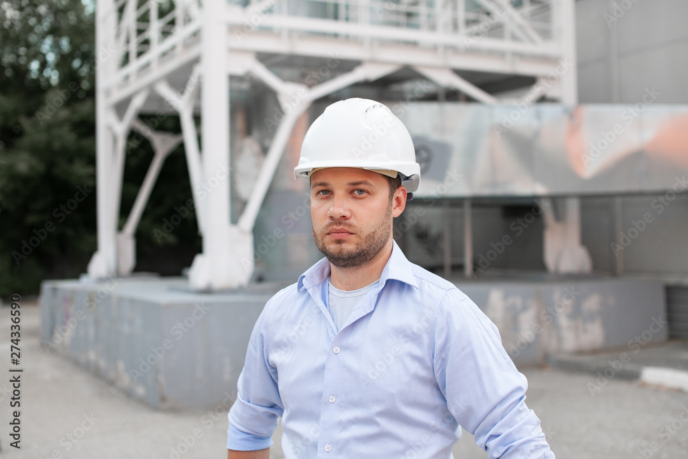 Young handsome male engineer in hardhat standing on the background of water or gas pipes. Concept of boiler station. Pipeline accessories closeup. Heating station manager doing his job outdoor. . Young handsome male engineer in hardhat standing on the background of water or gas pipes. Concept of boiler station. Pipeline accessories closeup. Heating station manager doing his job outdoor. .